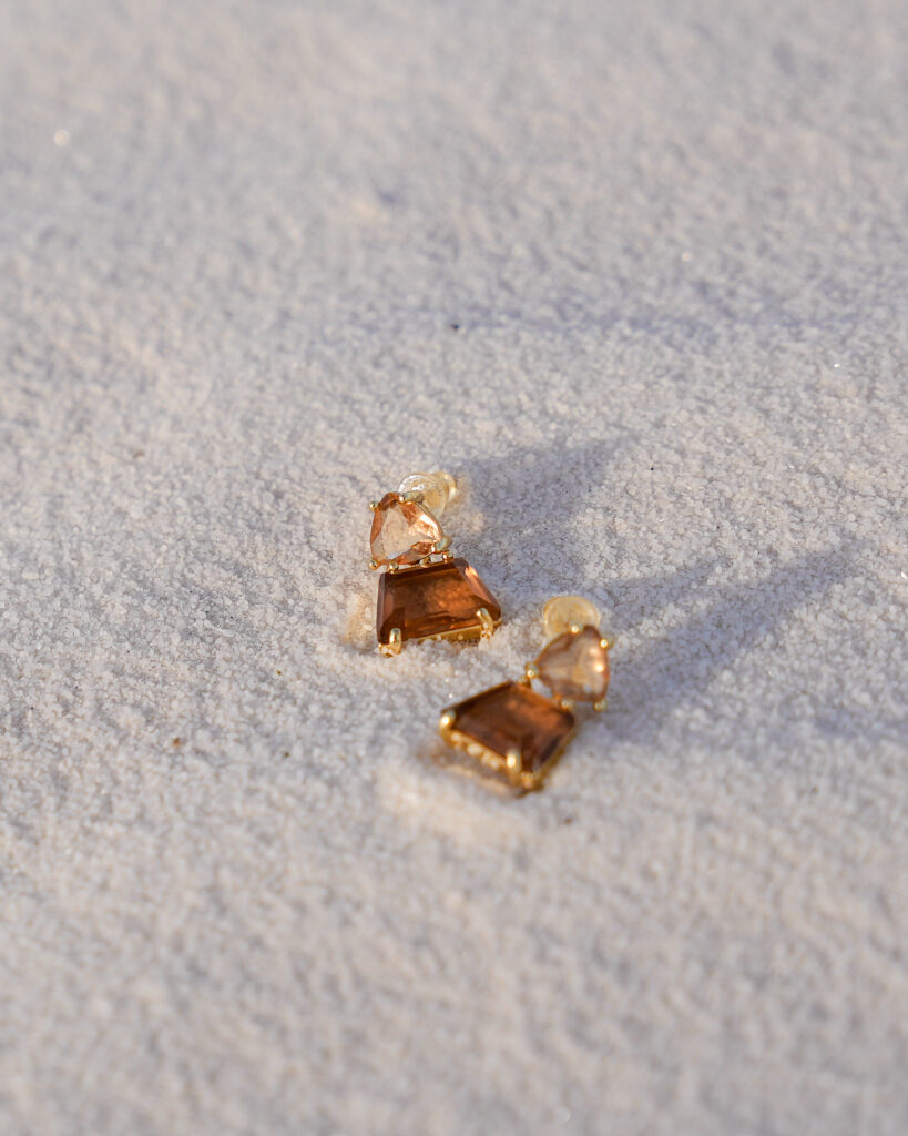 Minuit studio brand photography - close up on a high end earring jewelry made of gold and brown gemstones on a white sand dune at sunset