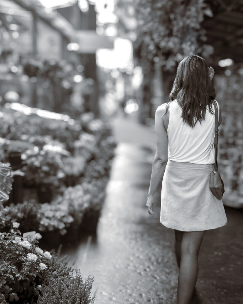 Minuit studio fashion photography - Black and white picture of a brunette women walking in the streets of Paris in the flower shops area wearing a skirt and a white top