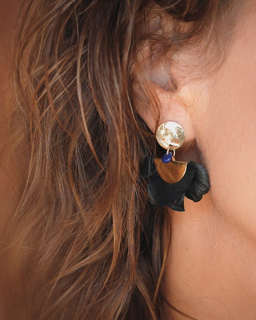 Minuit studio brand photography - close up on a high end earring jewelry made of gold and black flower petals on a brunette person with a brown caramel brackground for a French flair to fashion visuals